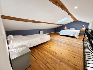 Ein Schlafzimmer mit zwei Betten, Holzboden, schrÀgen Deckenbalken und einem Oberlicht.