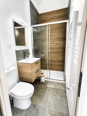 Ein modernes Badezimmer mit Toilette, Waschtisch, Spiegel, Dusche und einer Wand mit Holzverkleidung.