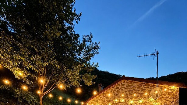 A stone building with a patio area, outdoor seating, and string lights. - The little landmark (Jujurieux)