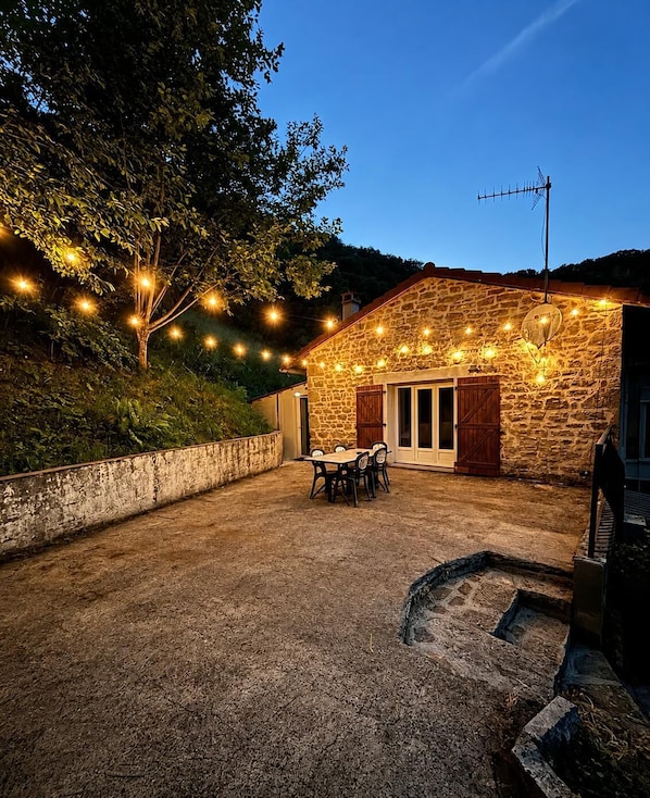Un edificio de piedra con un patio, asientos exteriores y luces colgantes.