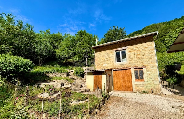 Una casa de piedra con puerta y ventana de madera, rodeada de vegetación y una escalera de piedra.