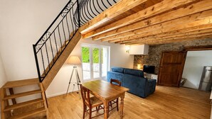 A wooden staircase with a metal railing, a dining table with chairs, a blue sofa, a stone fireplace, and a kitchen area with a refrigerator. - The little landmark (Jujurieux)