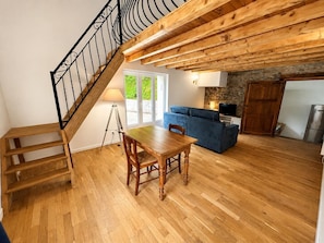 Una escalera de madera, una mesa de comedor, un sofá, una pared de piedra y una zona de cocina.