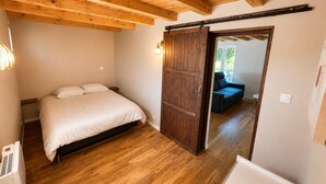 A bedroom with a wooden ceiling, a bed, a sliding door, and a view to a living area. - The little landmark (Jujurieux)