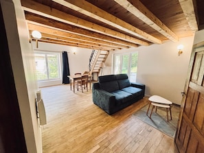 A spacious room with wooden floors, a black sofa, a dining table, and a staircase leading to an upper level.