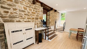 A room with a stone wall, wooden floor, a white cabinet, a staircase, and a view of greenery outside. - The little landmark (Jujurieux)