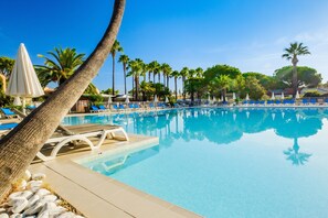A clear swimming pool with lounge chairs and umbrellas, surrounded by palm trees. - Chic Riverfront Stay With Balcony (Mandelieu-La-Napoule)