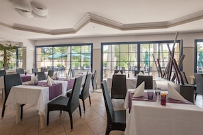 A restaurant with tables set for dining, chairs, and large windows with views of the outdoors. - Chic Riverfront Stay With Balcony (Mandelieu-La-Napoule)