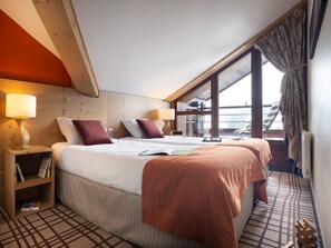 Ein Hotelzimmer mit einem großen Bett, zwei Nachttischen mit Lampen, einem Bücherregal und Blick ins Freie.