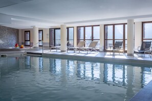 Ein Hallenbad mit Liegestühlen und großen Fenstern.