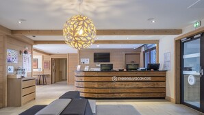 A reception desk with a wooden design and a logo, a waiting area with cushioned seating, and a large decorative light fixture. - Mountainside Suite With Hot Tub (Araches-la-Frasse)