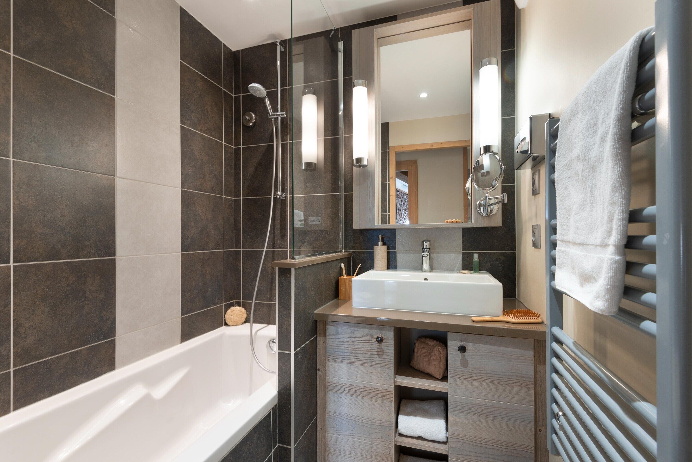 A modern bathroom with a bathtub, a sink, a mirror, and a towel rack.