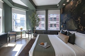 Habitación de hotel moderna con una cama grande, un escritorio, una planta en maceta y vistas a la ciudad.