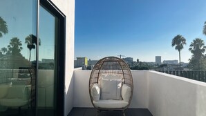 Un balcon avec un fauteuil en osier, un canapé et une porte vitrée.