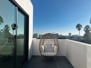 A balcony with a wicker chair, a sofa, and a glass door. - Luxe Silver Lake Home: Rooftop Terrace, Hollywood Views, 3BR/3.5BA, 2-Car Garage (Los Angeles)