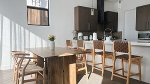 Une cuisine moderne avec des meubles de couleur bois foncé, un plan de travail blanc et une table à manger en bois assortie de chaises.