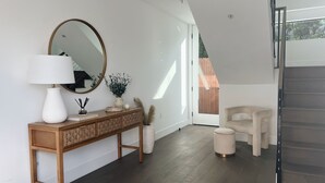 Un intérieur moderne avec une console en bois, un grand miroir, une lampe blanche, une plante en pot et un escalier.