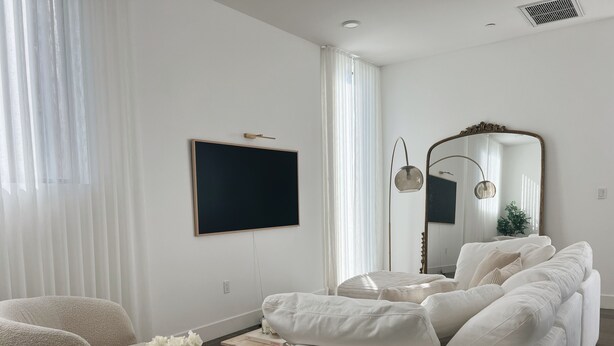 Un salon moderne avec un canapé blanc, une table basse ronde, un téléviseur à écran plat et un grand miroir.