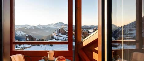 Un balcón con una mesa para dos, una silla y vistas a montañas nevadas.