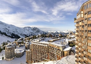 Eine verschneite Bergstadt mit mehrstöckigen Gebäuden, darunter ein Hotel mit Balkonen, und einem Skiort im Hintergrund.