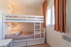 Ein Etagenbett mit einer Leiter, ein kleiner Tisch und ein Fenster mit Vorhängen.