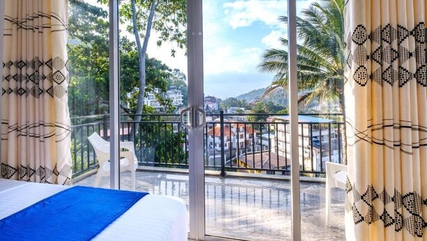 Ein Balkon mit einem Bett, einem Stuhl und Blick auf eine Stadtlandschaft.