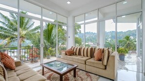 Ein großzügiger Wohnbereich mit Sofa, Couchtisch und großen Fenstern, die Blick auf Palmen und einen Balkon bieten.