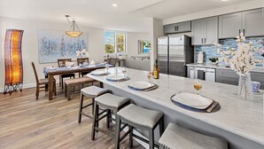 Una cocina moderna con una isla grande, taburetes de bar y un comedor con una mesa preparada para dos.