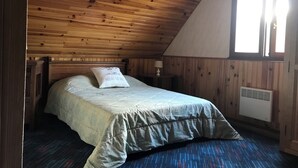 Una camera da letto con soffitto in legno, un letto con copripiumino decorato, un comodino con una lampada e una finestra con tende.