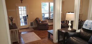 A living room with a leather couch, a small table with a lamp, a chair, and a door leading outside.
