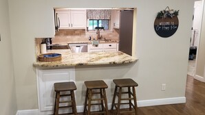 A kitchen with a marble countertop, white cabinets, and a 'Welcome to Our Happy Place' sign. - Lake Bridgeport Waterfront Charming Home with Private Dock / Boat & Jet Ski lift (Bridgeport)