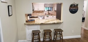 Una cocina con encimera de mármol, armarios blancos y un cartel que dice 'Welcome to Our Happy Place'.