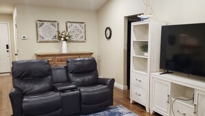 A living room with a black leather sofa, a white entertainment unit with a flat-screen TV, and a clock on the wall. - Lake Bridgeport Waterfront Charming Home with Private Dock / Boat & Jet Ski lift (Bridgeport)