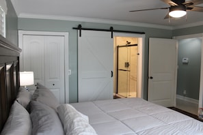 A bedroom with a bed, a ceiling fan, and a sliding door leading to a bathroom.