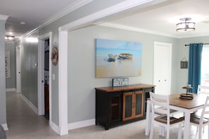 A dining area with a wooden table and chairs, a painting of boats on a beach, and a sign on the wall.