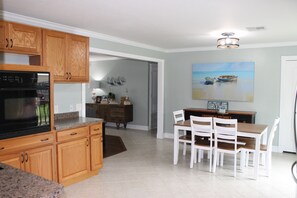 A kitchen with wooden cabinets, a granite countertop, and a dining area with white chairs and a wooden table.