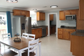 Une cuisine dotĂ©e de meubles en bois, dâun rĂ©frigĂ©rateur en acier inoxydable, dâun four Ă micro-ondes et dâun coin repas avec une table et des chaises.