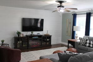 A living room with a flat-screen TV, a fireplace, a ceiling fan, and a sofa.