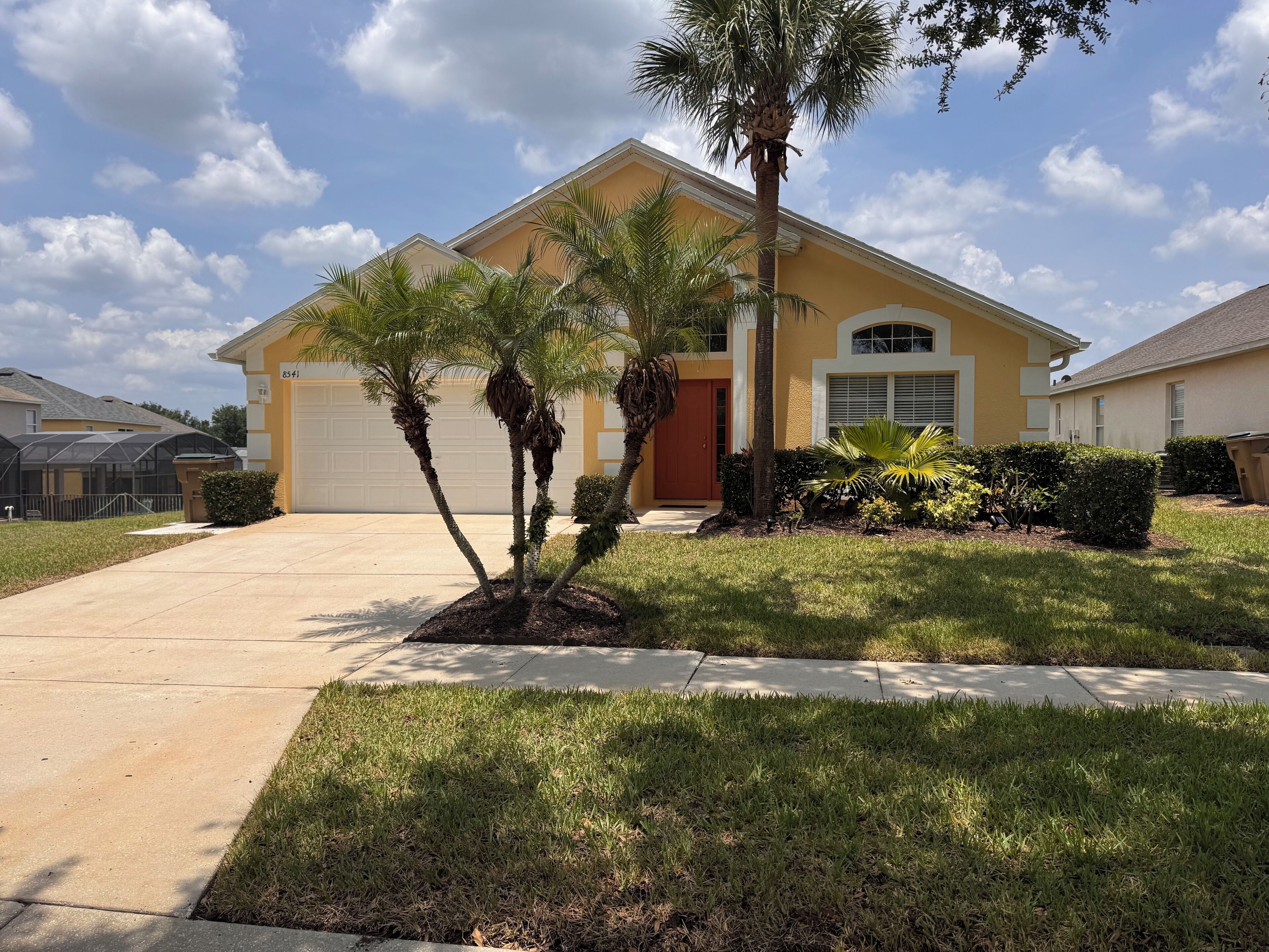 A residential house with a garage, palm trees, and a well-maintained lawn.