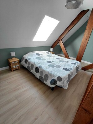 Une chambre avec un plafond en pente, un lit recouvert d’une couvre-lit à motifs, une table de chevet avec une lampe et un puits de lumière.