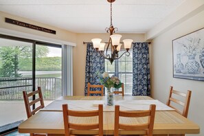 A dining area with a table, chairs, a chandelier, and a view through a window. - Charming 2-bedroom condo with many activities to do around the area. (Lake Harmony)
