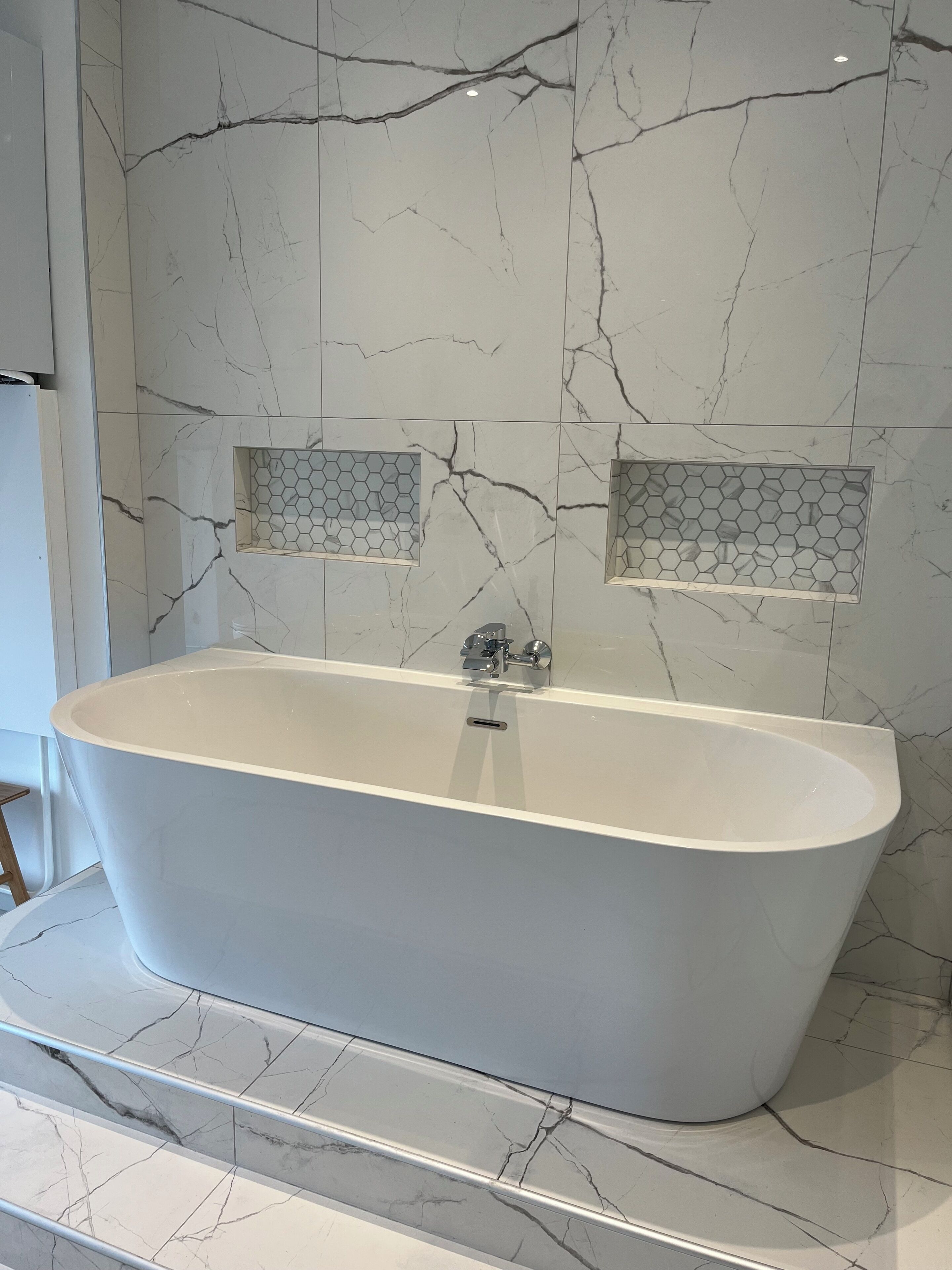 Ein modernes Badezimmer mit freistehender Badewanne, Marmorwänden und sechseckigen Flieserdetails.