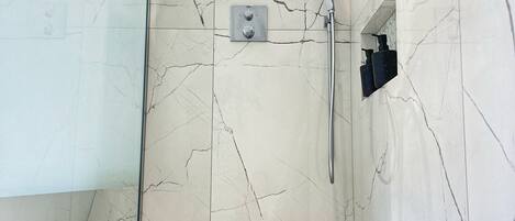 A modern bathroom with a glass shower enclosure, marble walls, and a built-in sink.
