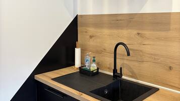 Een moderne keuken met een zwart aanrecht, houten spatwand en zwarte kastjes.