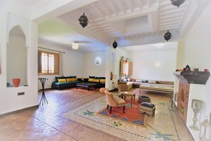 Un vaste espace de vie agrémenté d’un tapis à motifs, d’un ensemble de canapés, d’une table à manger et d’une cheminée.