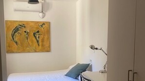 A small, neatly arranged bedroom with a bed, a desk, a chair, a painting, and a hanging light fixture. - Charming Flat in the heart of Barcelona (Barcelona)