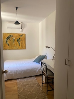 Een kleine, schone kamer met een bed, bureau, stoel, lamp en een schilderij aan de muur.