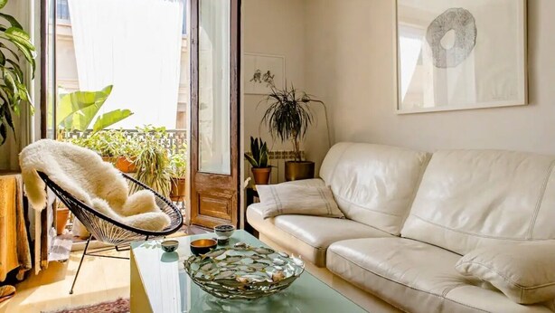 A living room with a white leather sofa, a white chair, a glass coffee table, and a potted plant. - Charming Flat in the heart of Barcelona (Barcelona)