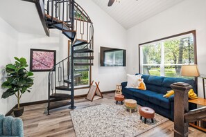 A modern living room with a spiral staircase, a blue sofa, a large window with blinds, and a potted plant.