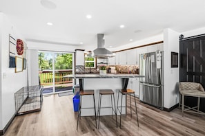 Una cocina moderna con una isla grande, electrodomésticos de acero inoxidable y un ventanal corredero a un balcón.